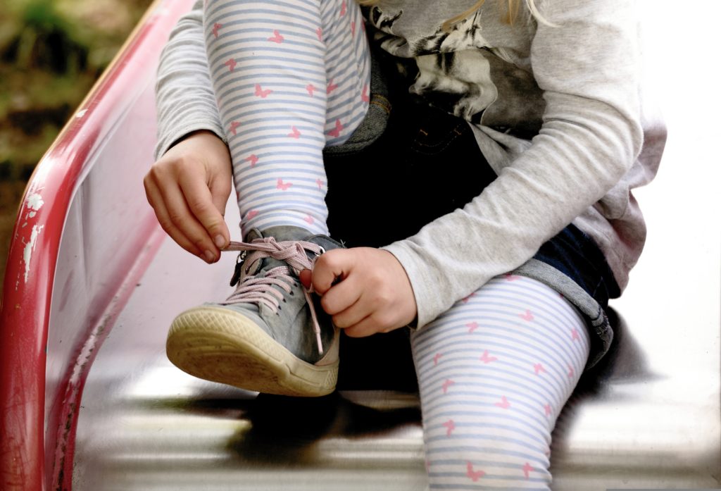 Kind bindet sich in der Kita auf der Rutsche die Schuhe zu